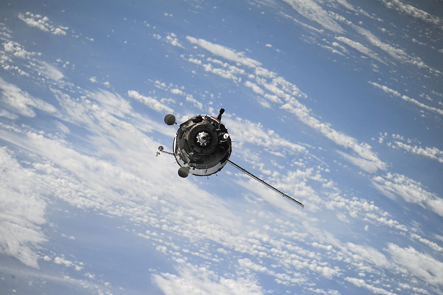 Spacecraft orbiting Earth with clouds and blue sky background