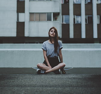 Young Woman Sitting Cross-Legged on Skateboard in Urban Setting