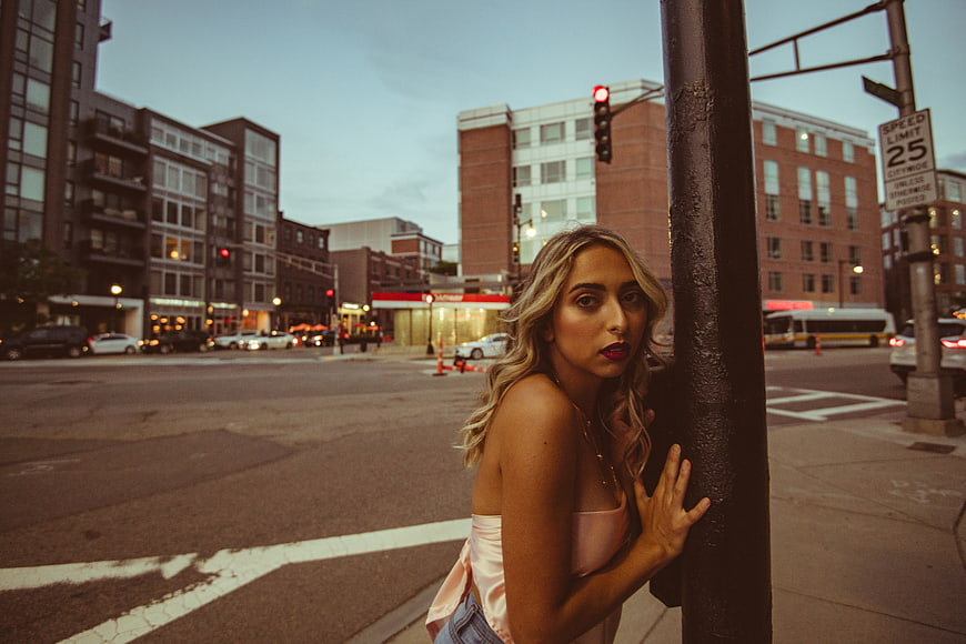 Blonde woman leaning on pole in urban street at dusk