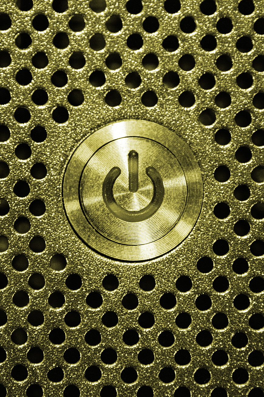 Close-up of gold power button on perforated metal texture