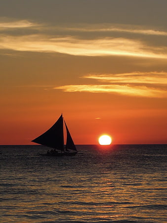Silhouette of traditional sailboat at sunset over ocean