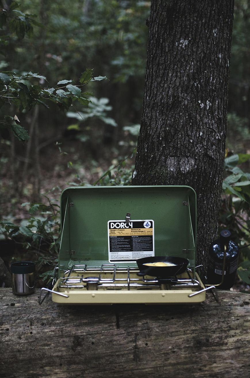 Vintage green camping stove cooking outdoors in forest