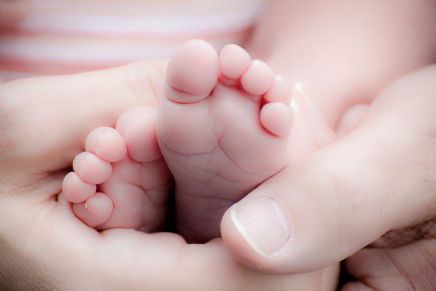 Close-up of newborn baby feet held in adult hands