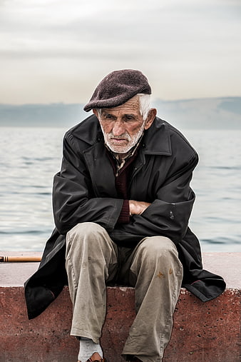 Portrait of elderly man sitting by the sea looking sad