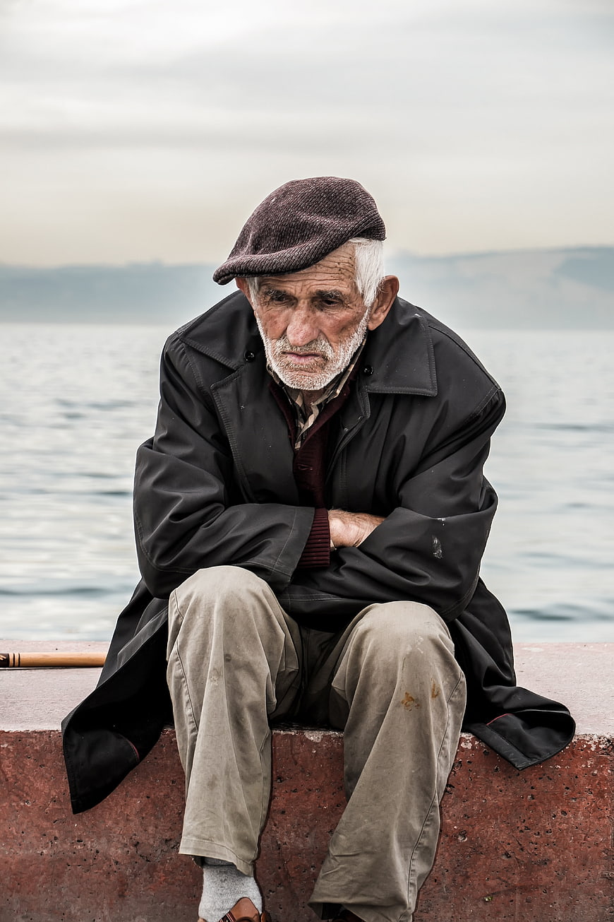 Portrait of elderly man sitting by the sea looking sad