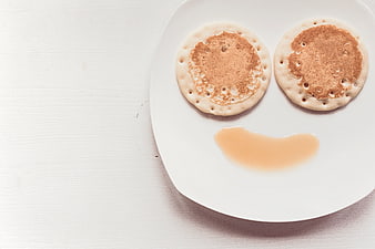 Pancakes arranged as a smiley face with syrup on white plate