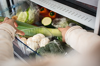 Hands organizing fresh vegetables in a refrigerator drawer