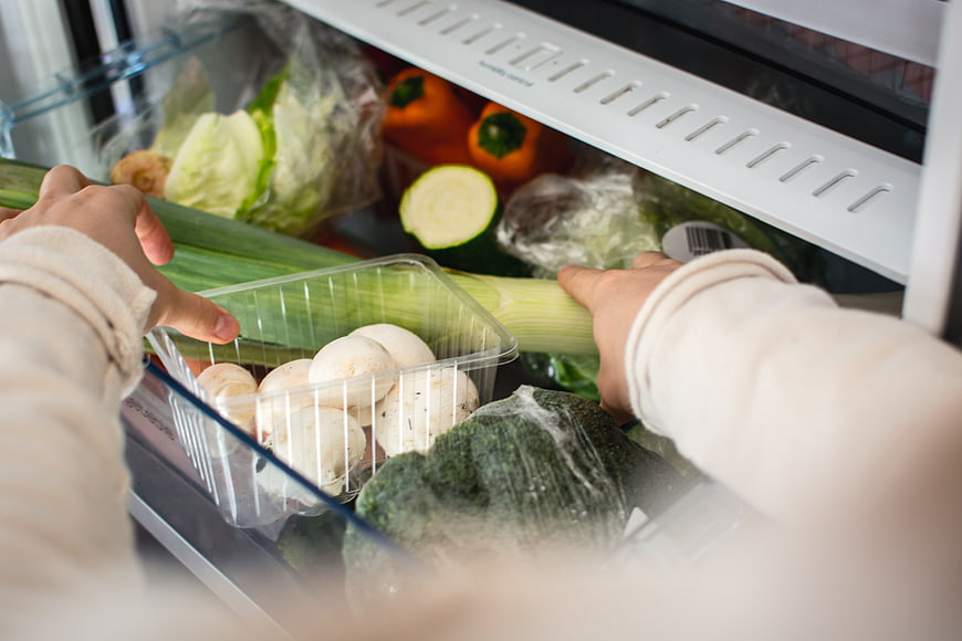 Hands organizing fresh vegetables in a refrigerator drawer