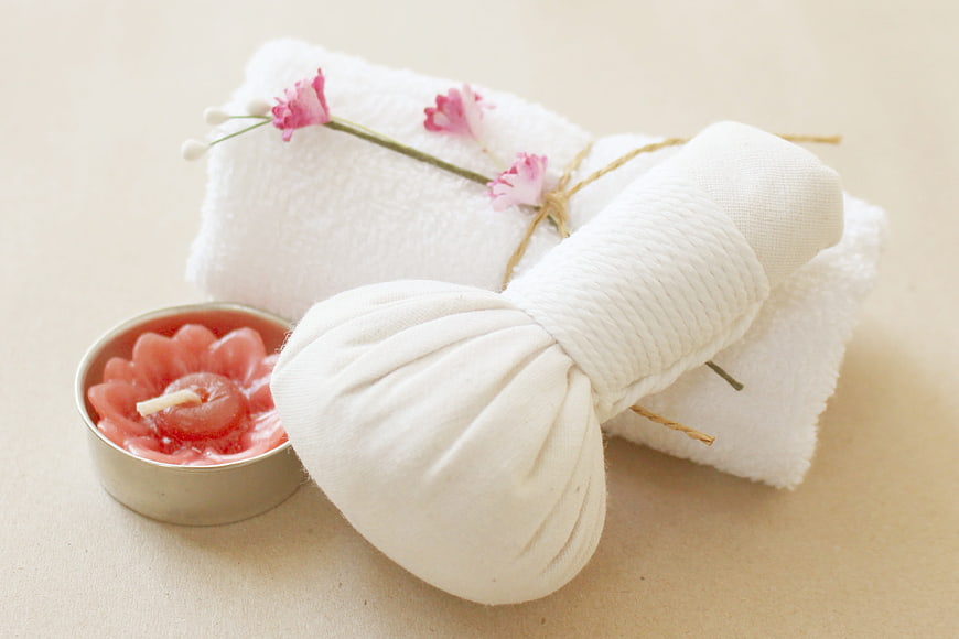 White herbal compress ball with pink flower and candle on beige background