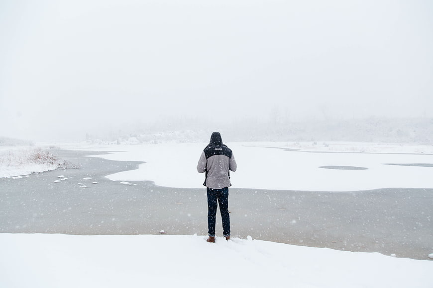 Man Standing Alone on Frozen River in Snowstorm
