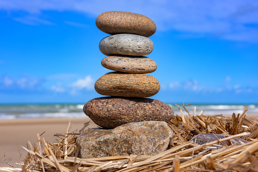 Stacked pebbles on straw at the beach with blue sky and ocean waves