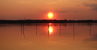 Serene Sunset Over Calm Lake with Silhouetted Wooden Poles
