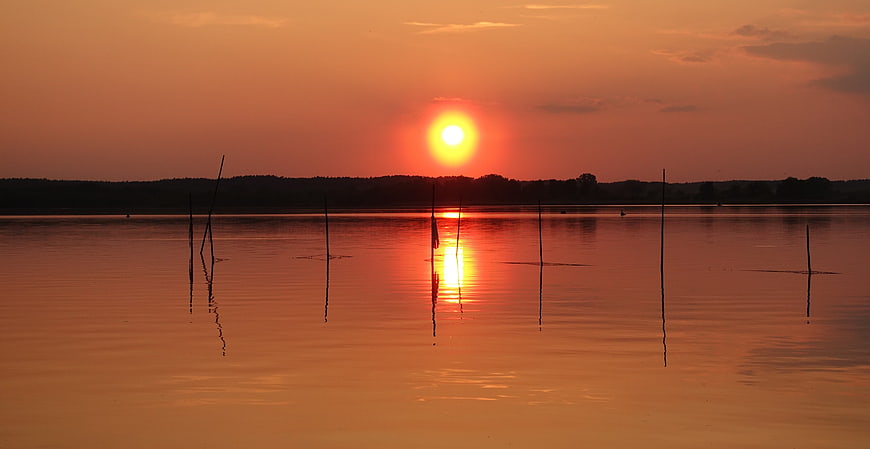 Serene Sunset Over Calm Lake with Silhouetted Wooden Poles