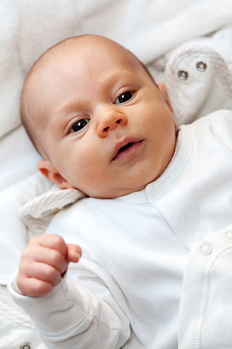 Close-up of newborn baby in white onesie lying on bed
