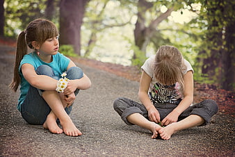 Two young girls sitting on a path in a park