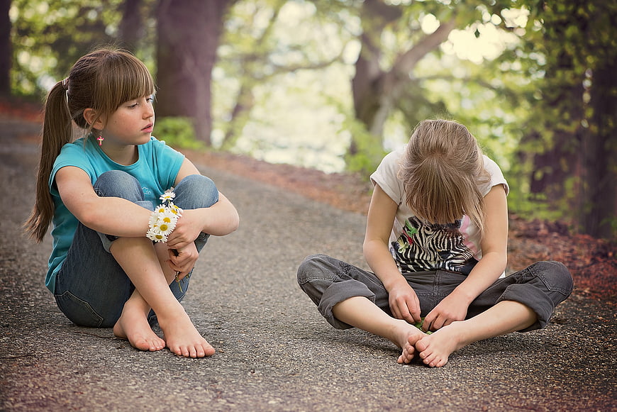 Two young girls sitting on a path in a park