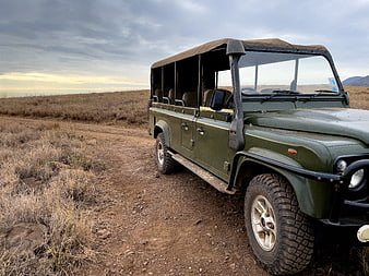 Green safari jeep parked on dirt road in dry savanna