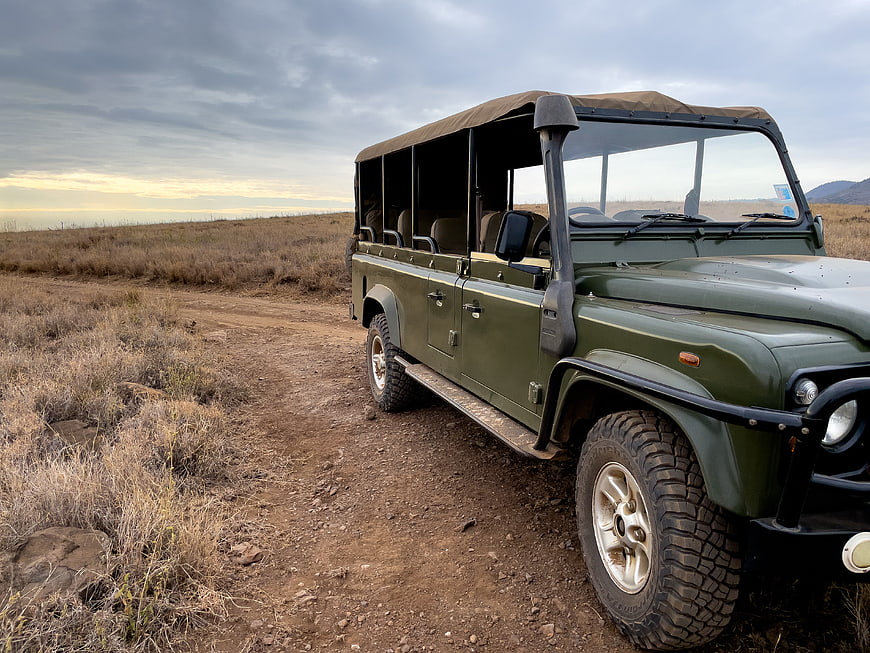 Green safari jeep parked on dirt road in dry savanna
