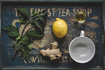 Flat lay of fresh mint, lemon, ginger, and tea cup on rustic tray