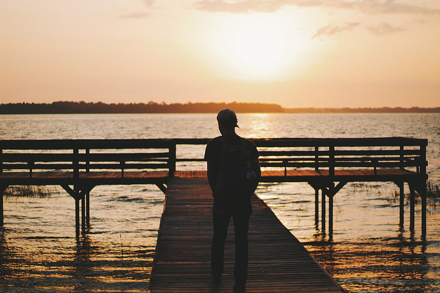 Silhouette of Man Standing on Wooden Pier at Sunset