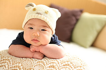 Cute Asian baby wearing a knitted bear hat resting on a lace blanket