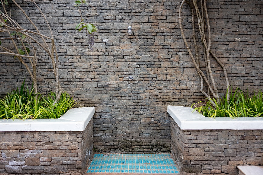 Outdoor stone shower with blue mosaic tiles and green plants