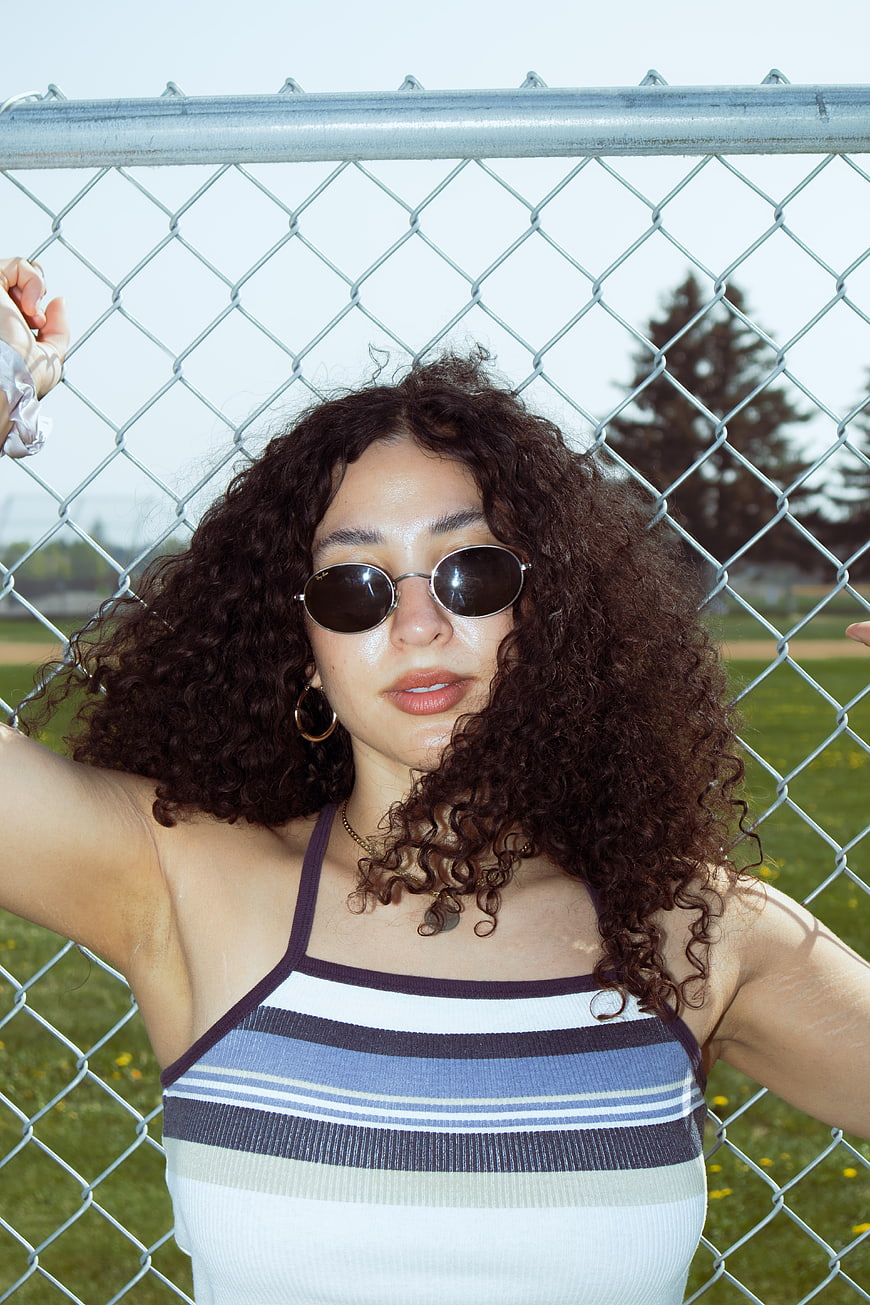 Young woman with curly hair and sunglasses leaning on fence