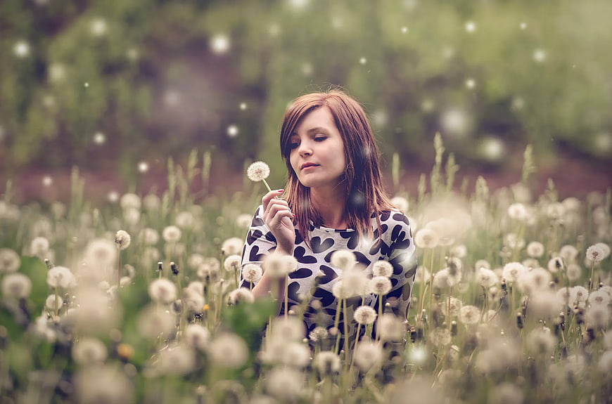 Woman Blowing Dandelion Seeds in a Field