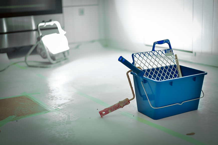 Blue paint bucket and roller on taped floor during renovation