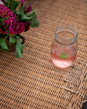 Pink cocktail in mason jar with flowers on wicker mat