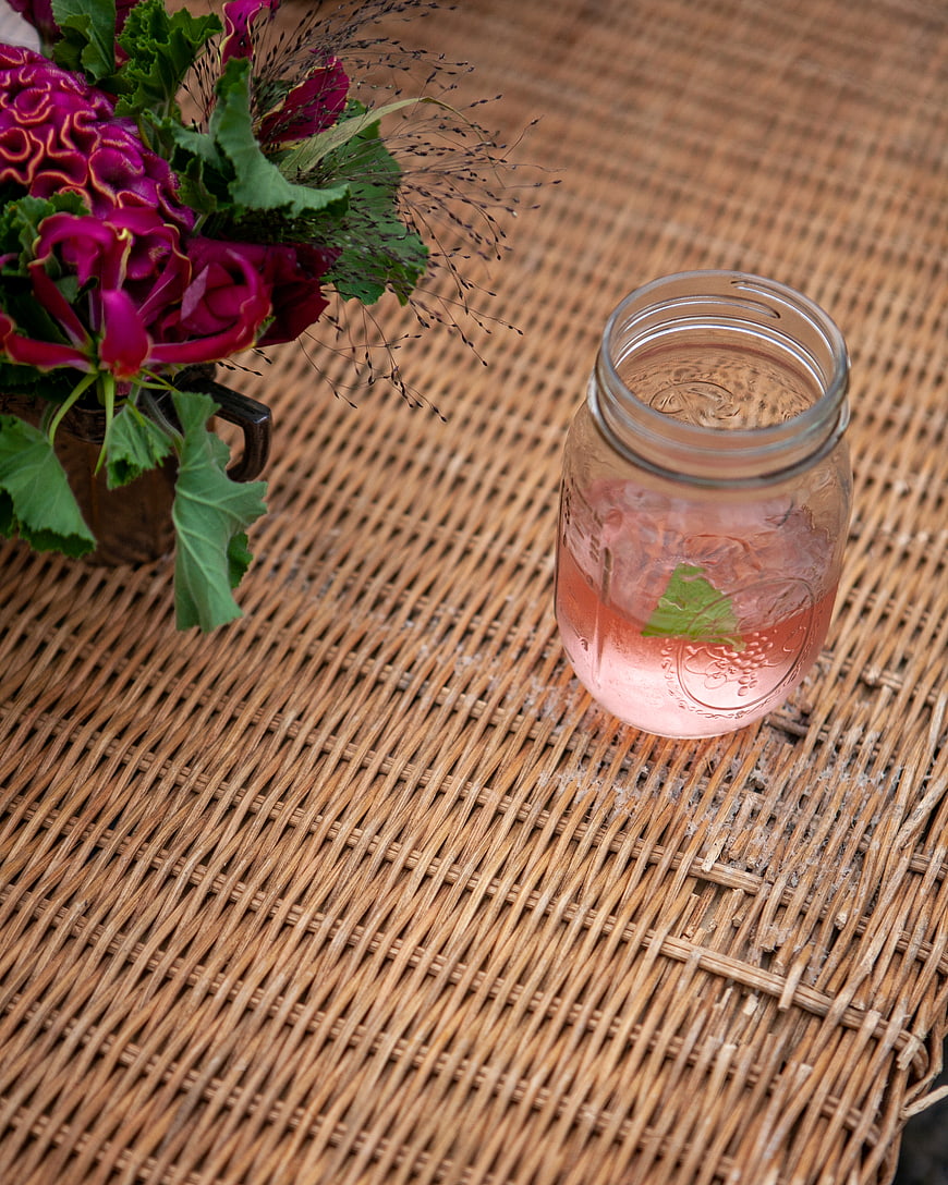 Pink cocktail in mason jar with flowers on wicker mat