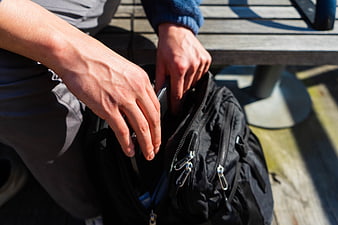 Close-up of hands packing a black backpack outdoors