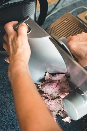 Close-up of hands slicing roast beef with electric meat slicer