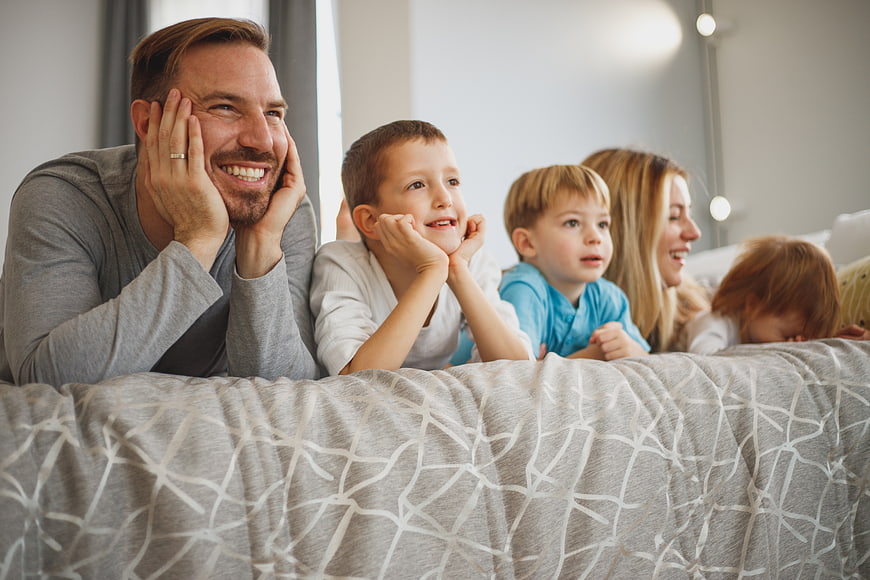 Happy family lying in bed watching TV together