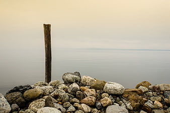 Minimalist wooden post on rocky shore with calm water