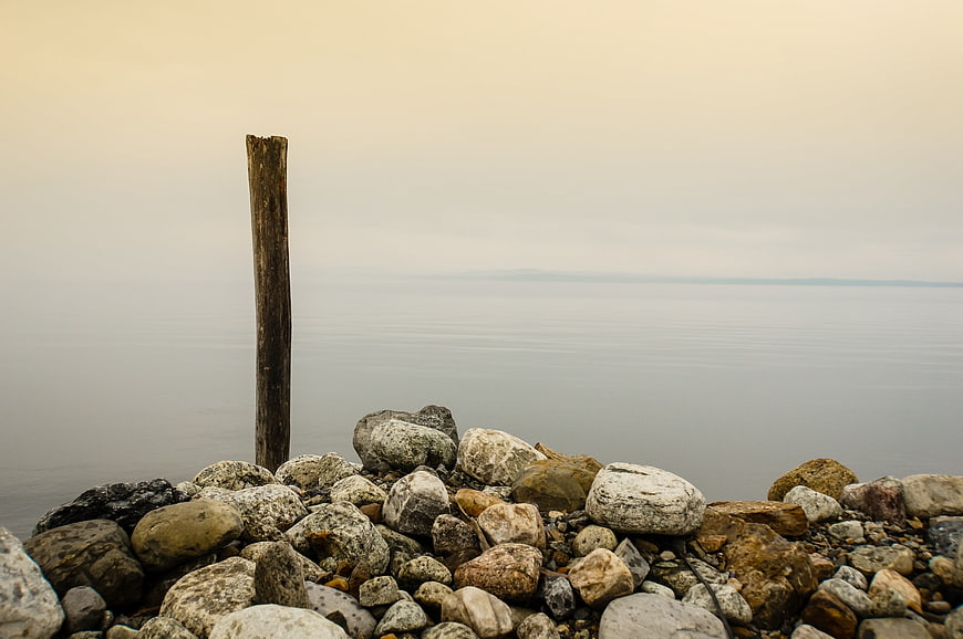 Minimalist wooden post on rocky shore with calm water