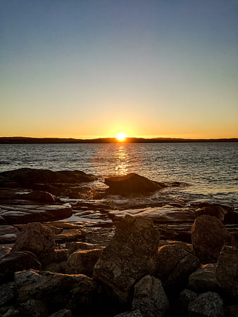 Sunset over rocky coastline with golden sun reflection on water