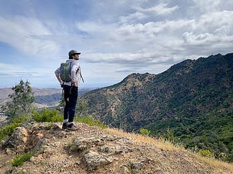 Hiker with Backpack Standing on Mountain Ridge Overlooking Valley