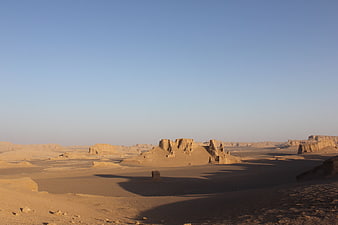 Vast desert landscape with sand dunes and rock formations under blue sky
