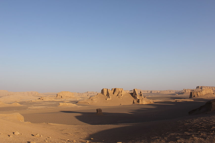 Vast desert landscape with sand dunes and rock formations under blue sky