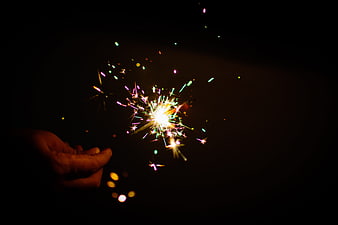 Hand holding colorful sparkler against dark night background
