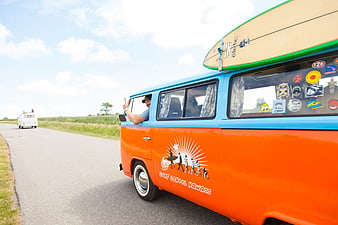 Vintage Orange VW Bus with Surfboard on Coastal Road