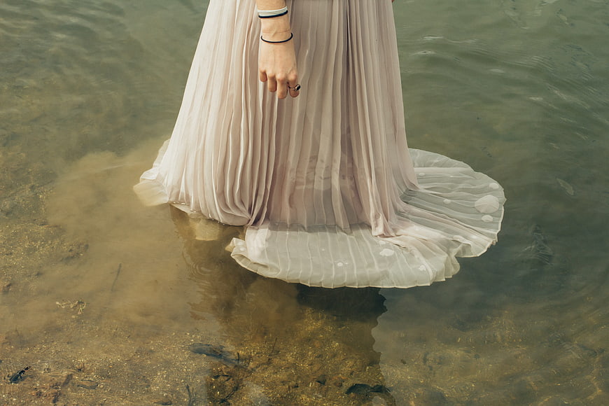 Woman in flowing beige dress standing in shallow water