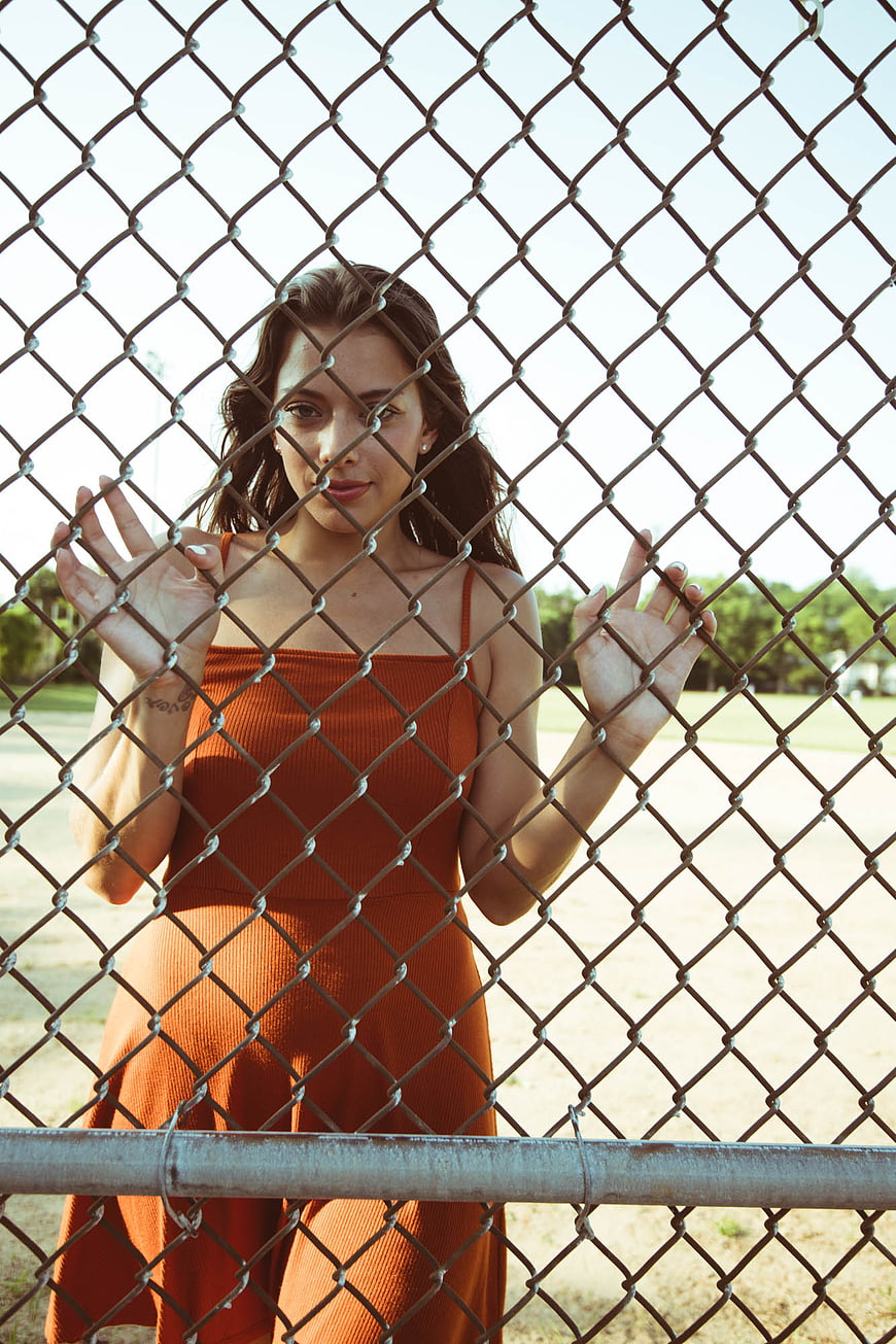 Woman in Orange Dress Behind Chain Link Fence