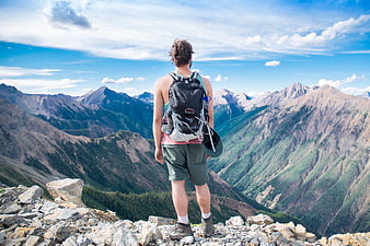 Hiker with Backpack Standing on Rocky Mountain Peak Overlooking Valley