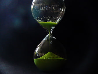 Green sand hourglass on dark background symbolizing time