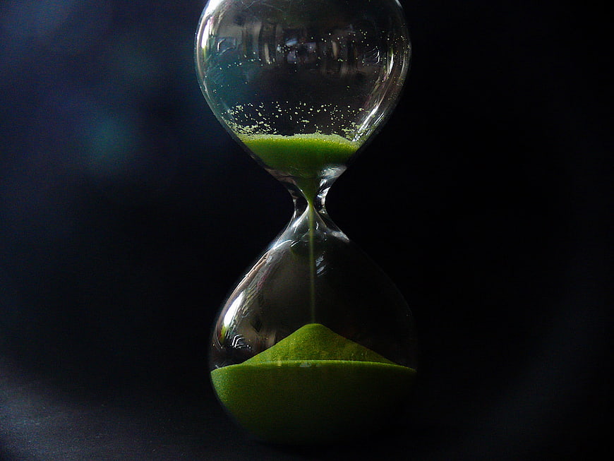 Green sand hourglass on dark background symbolizing time