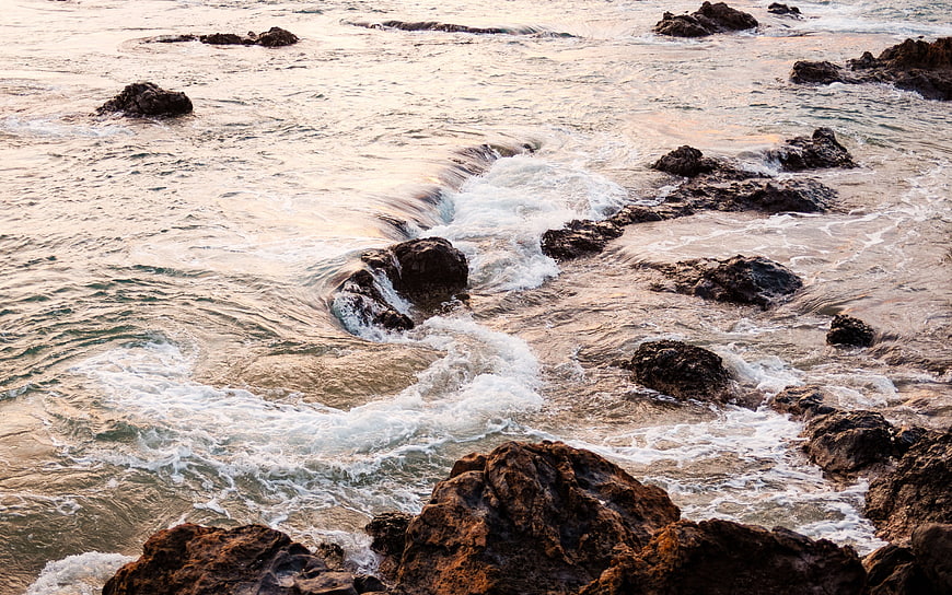 Ocean waves crashing on rocky shore at sunset