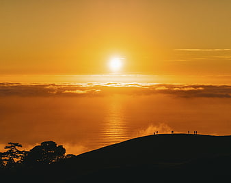 Silhouetted Hikers on Hilltop at Golden Sunset Over Ocean