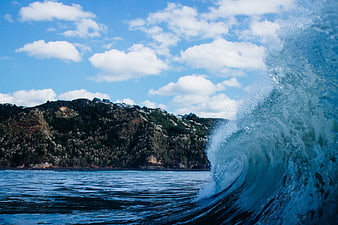 Curling ocean wave crashing near coastal hillside landscape